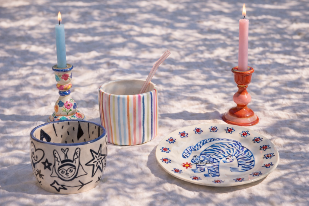 tafel met hand beschilderde keramiek. Er staan kandelaars, mokjes en een bord.