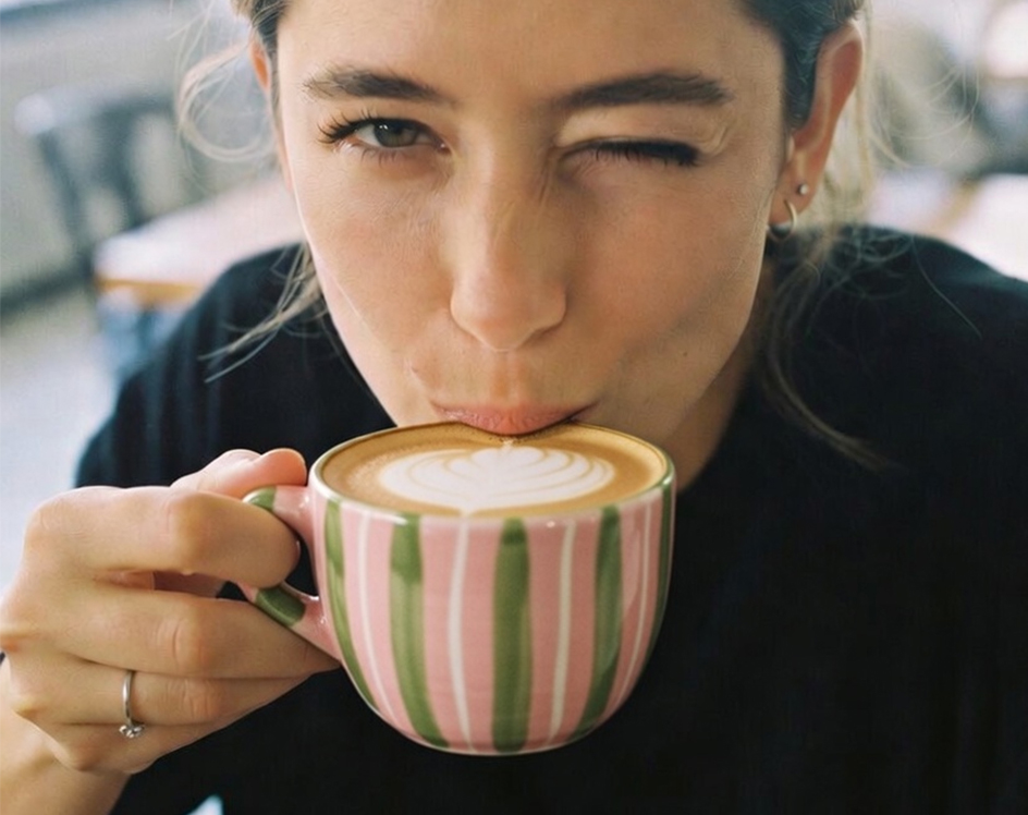 een vrouw drinkt een cappuccino uit haar zelf beschilderde kopjoe